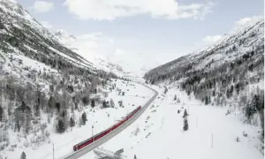 Un treno rosso attraversa una valle innevata, un viaggio tra i **treni panoramici Italia** con montagne maestose e alberi spogli.