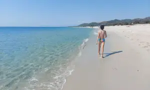 Bambino cammina sulla spiaggia della costa est Sardegna, mare cristallino e cielo azzurro.