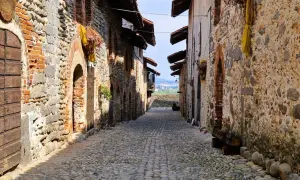 Antico vicolo lastricato nel ricetto di Candelo, con case in pietra e mattoni, archi e porte in legno.