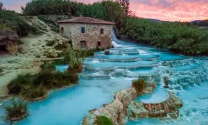 Cascate termali turchesi con un antico mulino in pietra, uno dei tanti posti belli in Toscana, al tramonto.