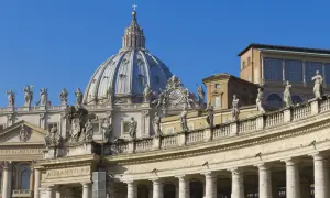 Cupola maestosa e colonnato di San Pietro, una delle quattro basiliche di Roma, con statue che vegliano sul cielo azzurro.
