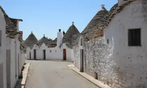 Strada tra i trulli, un incantevole esempio dei borghi da visitare in Puglia. Case bianche con tetti conici in pietra sotto un cielo azzurro.
