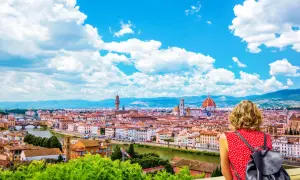 Una donna ammira il panorama di Firenze, la capitale della Toscana, con il Duomo e il Ponte Vecchio sotto un cielo azzurro e nuvoloso.