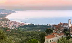 Panoramica di borghi del Cilento da visitare, con case arroccate su colline verdi che scendono verso il mare azzurro.
