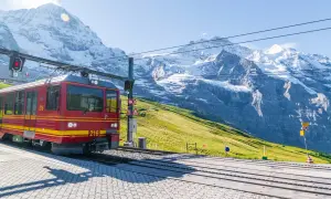 Treno rosso in montagna, pronto a salire tra vette innevate e verdi pendii.