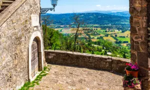 Un vicolo acciottolato a Bassano in Teverina conduce a un panorama mozzafiato di colline verdi e campi coltivati sotto un cielo azzurro.