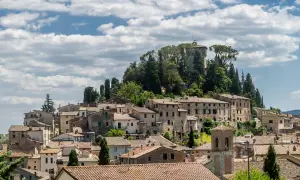 Panoramica di Cetona, un borgo toscano arroccato su una collina, con case in pietra e tetti in cotto sotto un cielo nuvoloso.