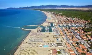 Vista aerea di una località balneare in provincia di Grosseto, con spiaggia attrezzata, porto turistico e case con tetti rossi.
