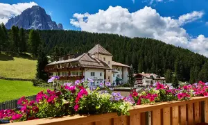 Fiori colorati su un balcone con vista su un hotel e le montagne, un'oasi di pace nei rifugi Val Gardena.