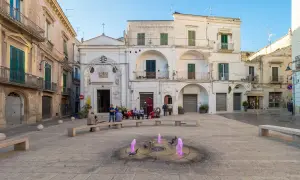 Piazza nel gravina in puglia centro storico con fontana rosa e persone sedute.