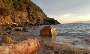 Spiaggia di Cala del Gesso al tramonto, con scogli dorati e un tronco sulla riva.