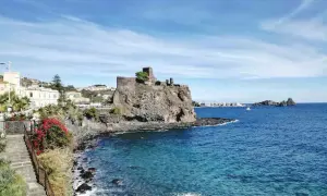 Castello normanno su scogliera lavica, un gioiello tra le cose da vedere a Catania e dintorni. Mare azzurro e case bianche.