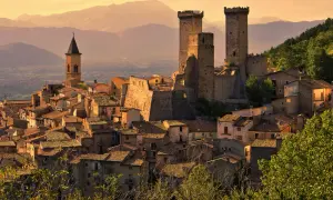 Borghi da visitare in Abruzzo: un castello medievale domina un villaggio arroccato, con torri imponenti e case in pietra sotto un cielo dorato.