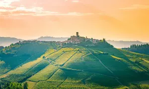 Colline vitate al tramonto nelle Langhe, Roero e Monferrato, con un borgo arroccato e un castello.
