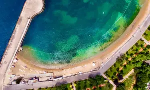 Vista aerea di una spiaggia e di un molo a Istanbul, dove c'è il mare turchese e una strada costiera con un parco verde.