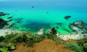 Vista dall'alto di una baia con acqua cristallina e spiagge dorate, tra le spiagge più belle della Calabria. Rocce e vegetazione mediterranea incorniciano il paesaggio.