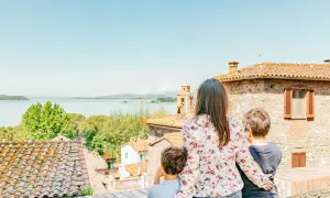 Una madre e due bambini ammirano un lago e un borgo italiano, scoprendo luoghi magici per bambini in Italia.