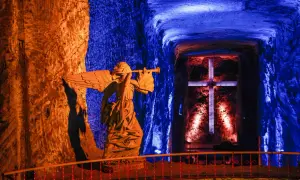 Statua di un angelo con tromba nella cattedrale del sale, illuminata da luci blu e arancioni, con una croce sullo sfondo.
