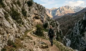 Escursionista su un sentiero roccioso, con un antico edificio incastonato nella roccia. Un viaggio che sembra un vero sentiero dello spirito tra montagne maestose.