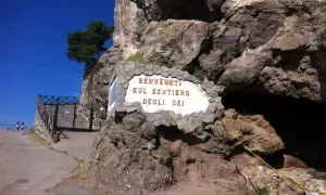 Benvenuti sul Sentiero degli Dei, un'iconica insegna incastonata nella roccia, con un cancello e un sentiero che invitano all'avventura.
