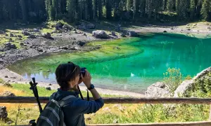 Donna con zaino e macchina fotografica cattura la bellezza del Lago di Carezza, un luogo imperdibile tra le meraviglie del Trentino Alto Adige cosa vedere.