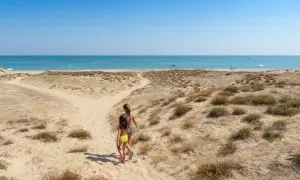 Due bambine corrono verso il mare in Abruzzo, tra dune sabbiose e macchia mediterranea.