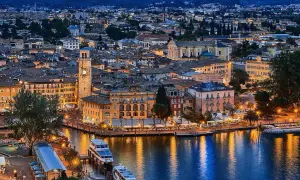 Incantevole vista serale di un borgo sul lago, con edifici colorati, un campanile e barche illuminate. Un gioiello tra i paesi del Trentino Alto Adige.