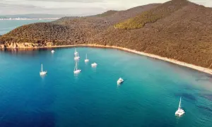 Vela al largo della costa della Maremma Toscana. Il mare azzurro e cristallino abbraccia una baia con diverse barche a vela e un catamarano.
