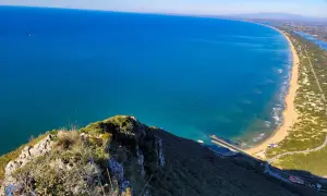 Vista dall'alto del promontorio del Circeo, con il mare azzurro, la spiaggia dorata e la vegetazione lussureggiante.