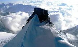 Il rifugio più alto d'Europa, un edificio scuro su una vetta innevata, domina un mare di nuvole e montagne.