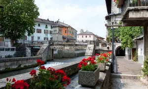 Un pittoresco canale attraversa il borgo Val Sugana, fiancheggiato da case colorate e gerani rossi in fiore.