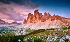 Le maestose cime di Lavaredo illuminate dal tramonto, con un cielo viola e blu che fa da sfondo a un paesaggio alpino mozzafiato.