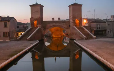 Ponte di barche a Comacchio, uno dei borghi medievali vicino a Ferrara, con le sue torri illuminate e il riflesso sull'acqua.