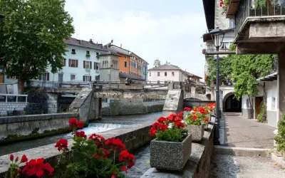 Un pittoresco canale attraversa il borgo Val Sugana, fiancheggiato da case colorate e gerani rossi in fiore.