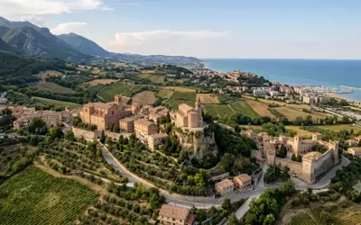 Borghi da visitare vicino Ascoli Piceno: un castello medievale e chiese storiche su colline verdi, con il mare all'orizzonte.