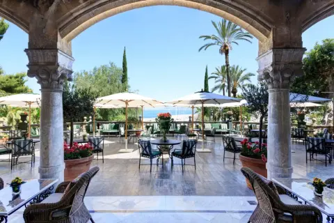 Terrazza con vista mare per un aperitivo a Palermo, tra palme e archi antichi.