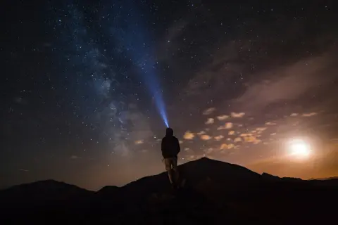 Persona su una montagna di notte, illuminata da una torcia, sotto un cielo stellato mozzafiato.