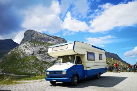 Camper blu e bianco parcheggiato in montagna, pronto per esplorare gli **itinerari camper Italia**. Due ciclisti sullo sfondo.