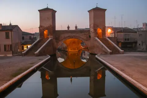Ponte di barche a Comacchio, uno dei borghi medievali vicino a Ferrara, con le sue torri illuminate e il riflesso sull'acqua.