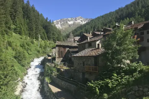 Un pittoresco borgo alpino nel Nord Italia, con case in pietra e tetti in ardesia, incastonato tra boschi rigogliosi e un torrente impetuoso.