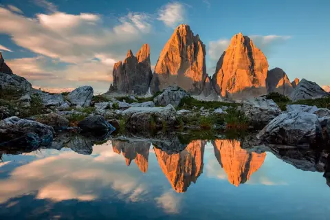 Le Tre Cime di Lavaredo illuminate dal tramonto, riflesse in uno specchio d'acqua. Le **dolomiti più belle** in uno scenario mozzafiato.