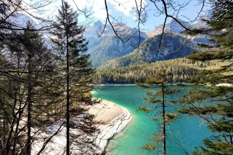 Un lago turchese incastonato tra montagne boscose, con una spiaggia sabbiosa che si estende nel **Val di Non**.