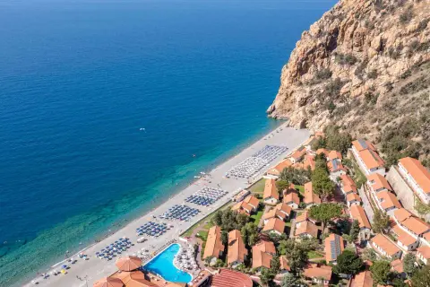 Villaggio turistico con spiaggia attrezzata e piscina, incastonato tra il mare blu e una scogliera rocciosa. Un luogo ideale per esplorare i paesi vicino Catania sul mare.