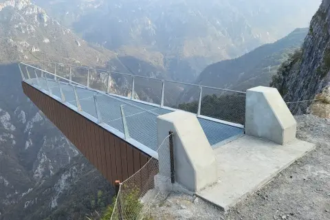 La passerella panoramica "Becco di Dossena" si protende su un profondo canyon, offrendo una vista mozzafiato sulle montagne circostanti.