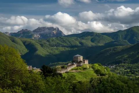 Roccia fortificata nella Garfagnana, dove si trova un castello medievale su una collina verdeggiante, con montagne sullo sfondo.