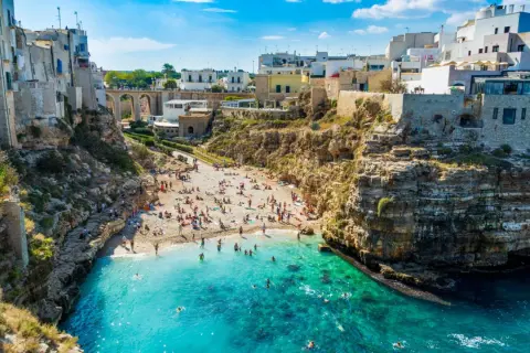 Una baia con spiaggia affollata e case bianche a picco sul mare turchese, una delle splendide spiagge vicino Bari.