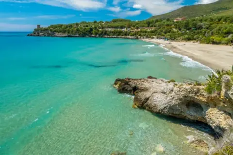 Spiaggia dorata e mare cristallino nel Cilento, uno dei posti più belli del Cilento mare, con una torre antica a picco sul blu.