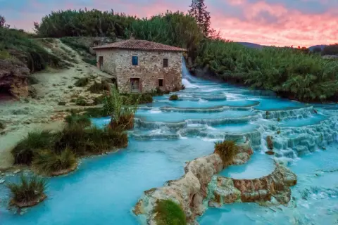 Cascate termali turchesi con un antico mulino in pietra, uno dei tanti posti belli in Toscana, al tramonto.