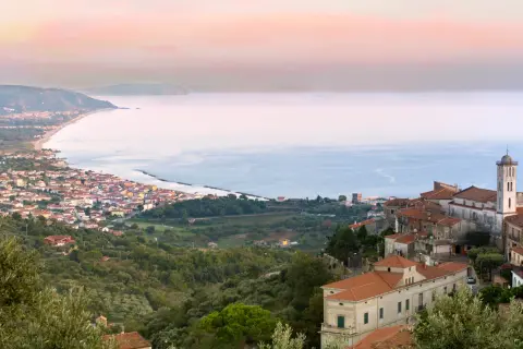 Panoramica di borghi del Cilento da visitare, con case arroccate su colline verdi che scendono verso il mare azzurro.