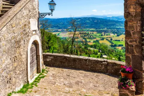 Un vicolo acciottolato a Bassano in Teverina conduce a un panorama mozzafiato di colline verdi e campi coltivati sotto un cielo azzurro.